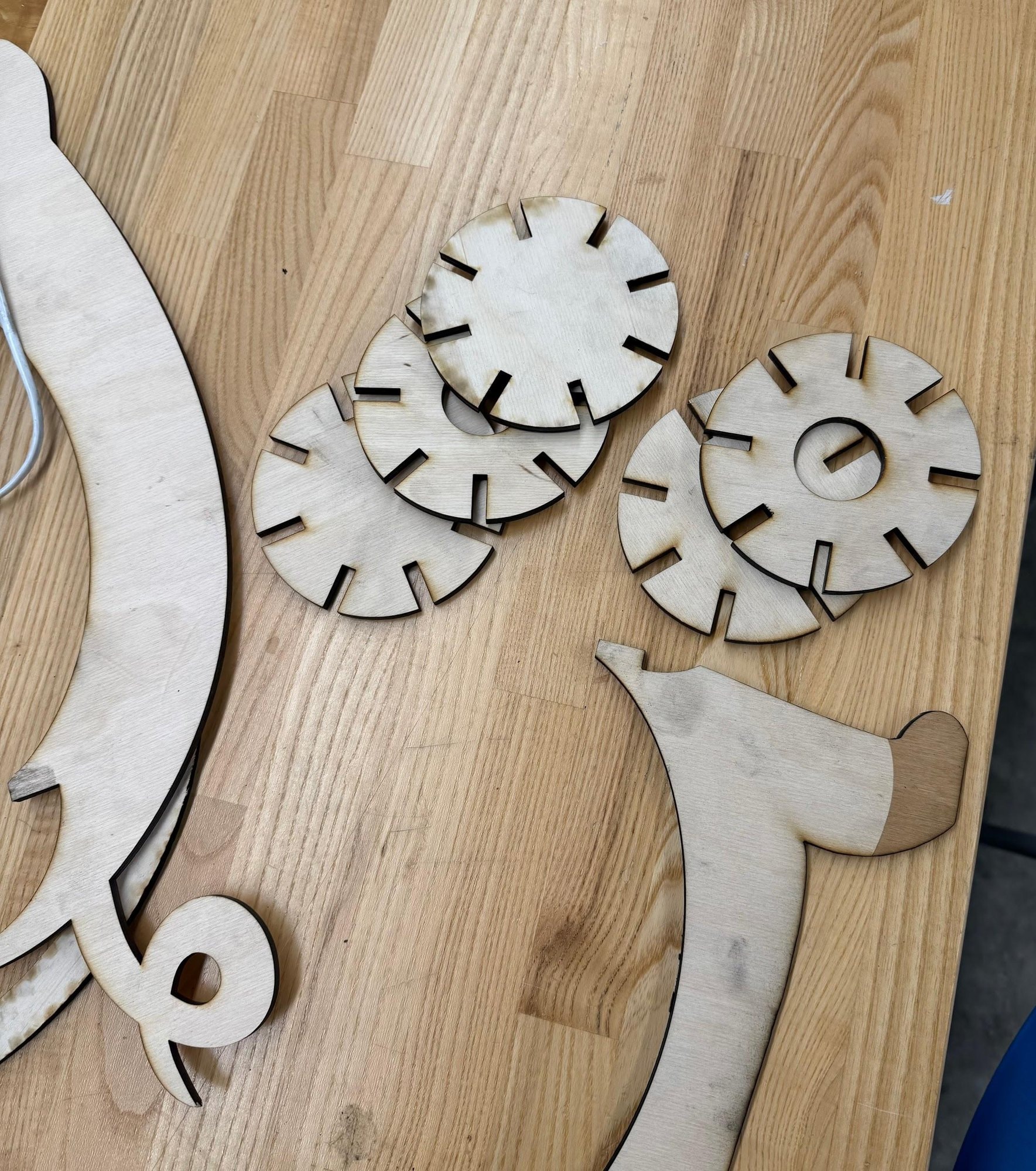 Draft laser-cut parts on a table: several slotted rings and a curved silhouette piece in raw wood.