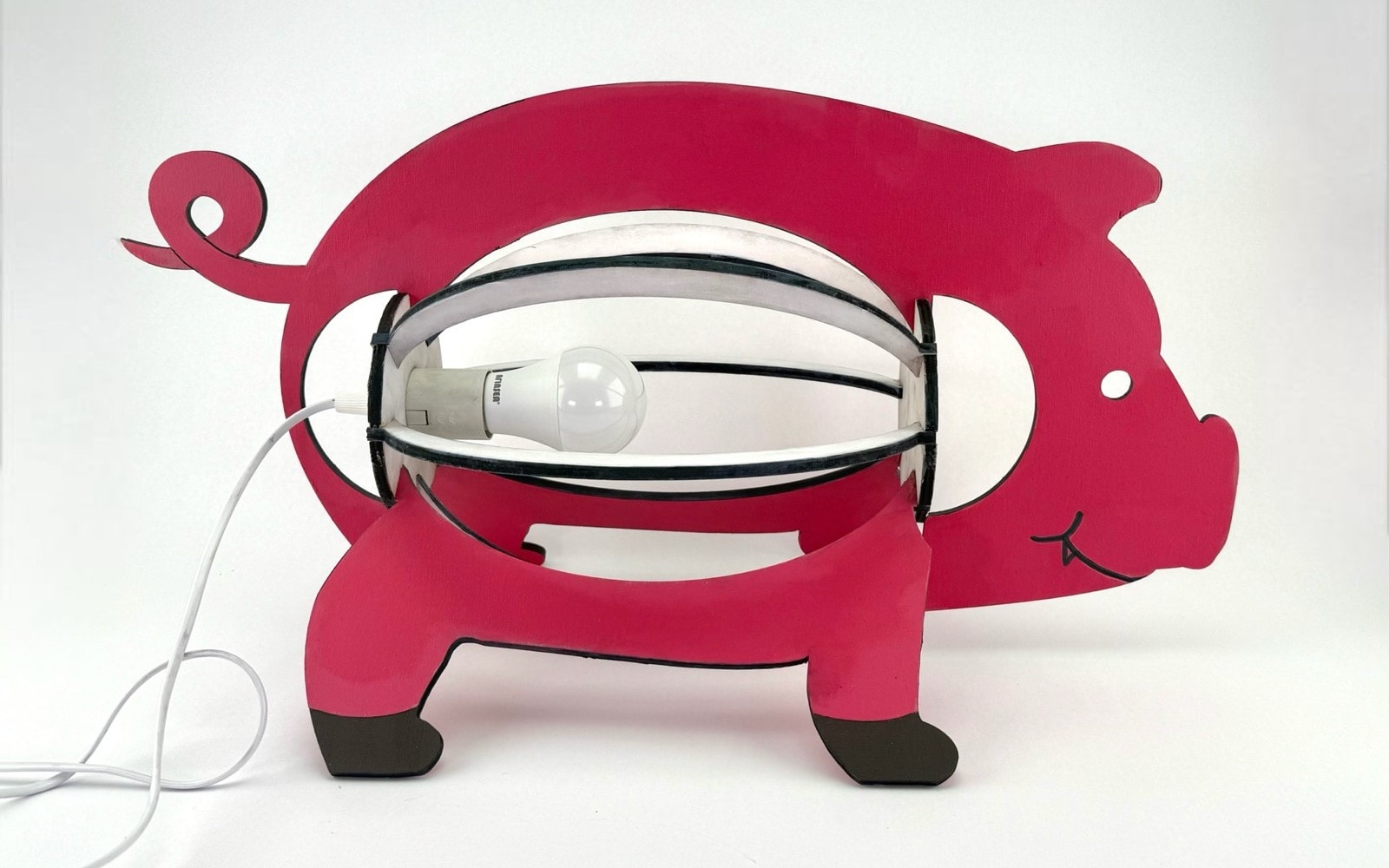 The pig lamp: a pink laser-cut wood pig silhouette whose body opens into a cage of curved ribs around a bulb.