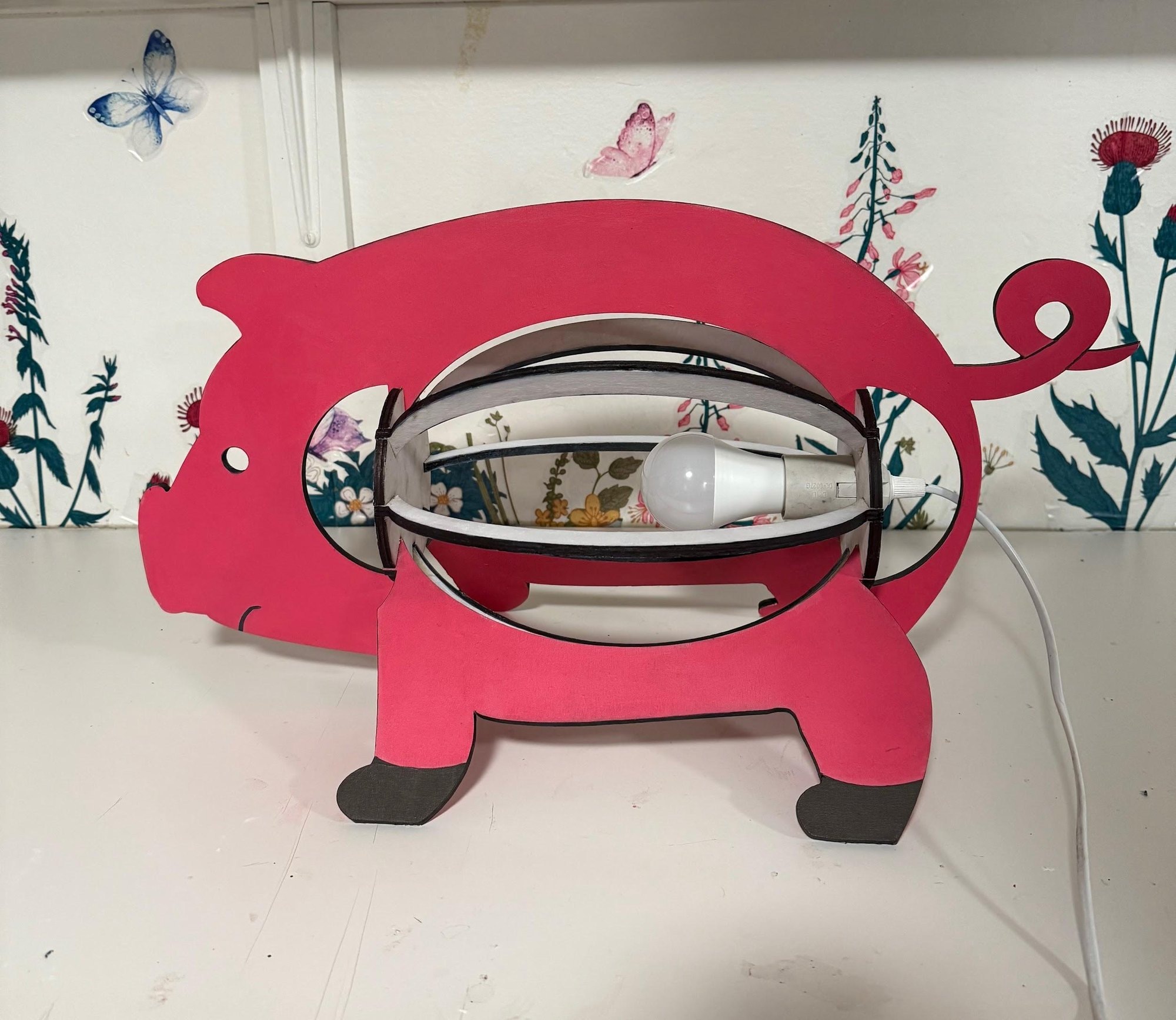 The finished lamp painted pink with dark hooves, seen from the side.